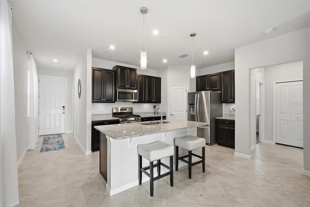 A kitchen features dark wood cabinets, granite countertops, a center island, and stainless steel appliances — 12261 BLUE PACIFIC DRIVE, RIVERVIEW, FL