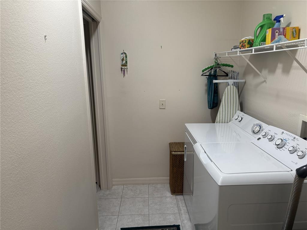 A laundry room features a white washing machine, a wire shelf, and tiled flooring — 420 GLEN ARBOR LANE, LEESBURG, FL