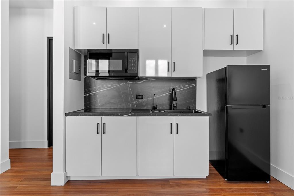A kitchen features white cabinets, a black refrigerator, a microwave, and a dark stone backsplash — 6951 C REINA ISABEL STE. 101 UNIT 3B Bolero, PONCE, PR