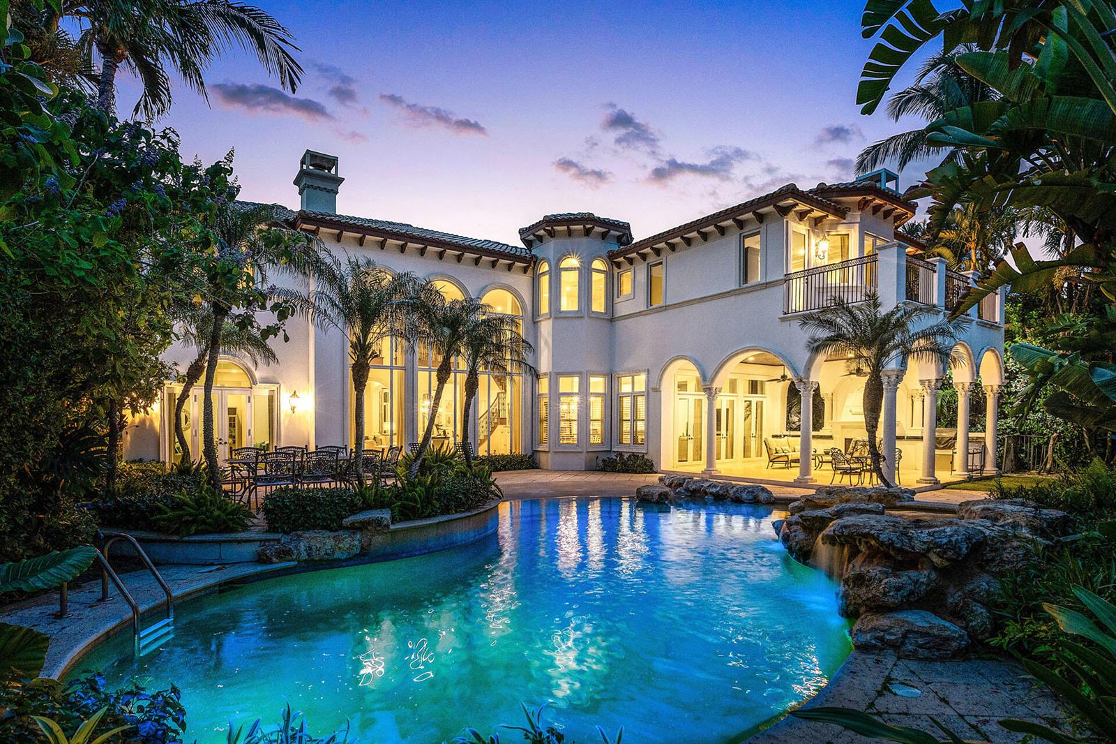 A two-story Mediterranean-style home features a backyard swimming pool with a rock waterfall at dusk — 1282 Sabal Palm Drive, Boca Raton FL 33432, BOCA RATON, FL