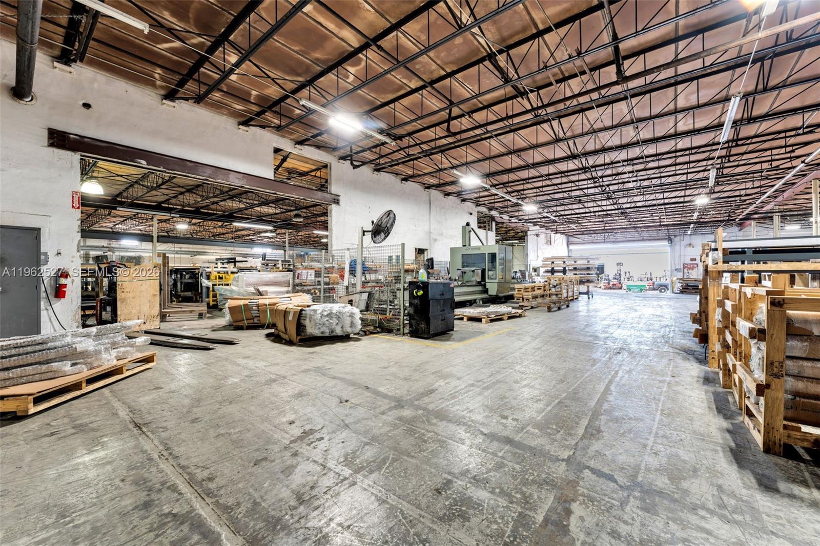 A large industrial warehouse features a concrete floor, exposed ceiling trusses, and stored materials — 315 W 75th Pl, Hialeah FL 33014, HIALEAH, FL