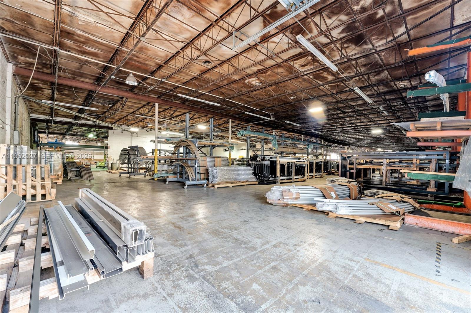 A large industrial warehouse space features exposed ceiling trusses, concrete floors, and metal storage racks — 315 W 75th Pl, Hialeah FL 33014, HIALEAH, FL
