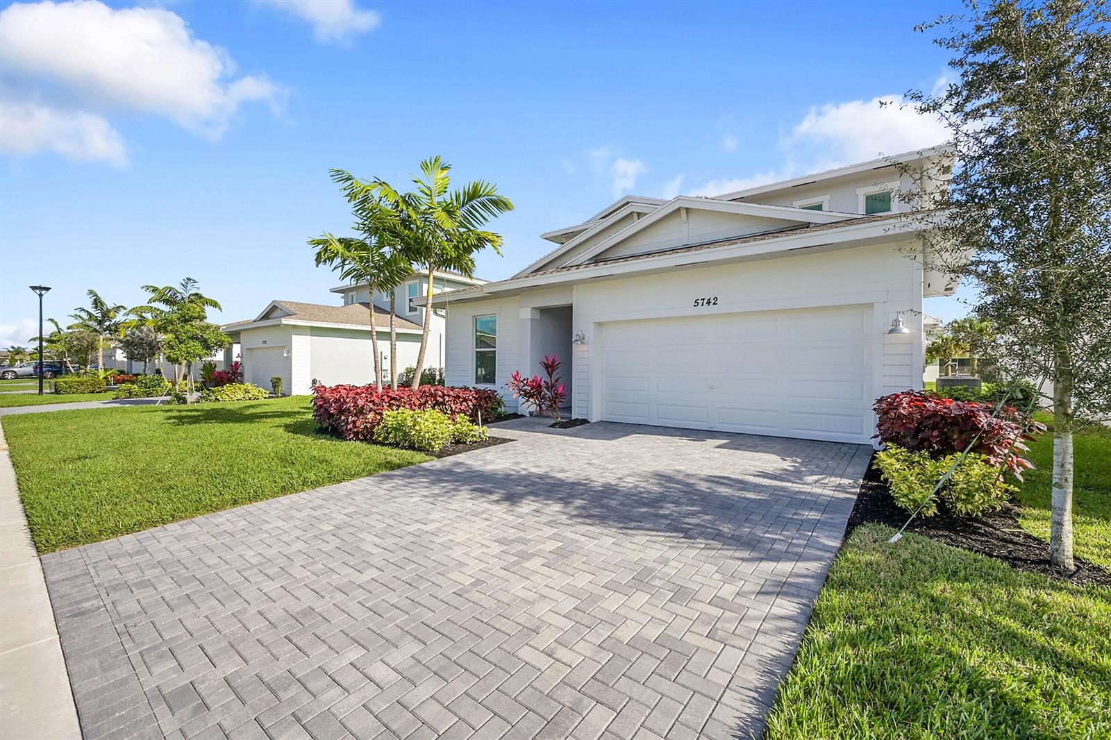 A white two-story house features a paved driveway, a two-car garage, and landscaped front gardens — 5742 Graceful Way, Delray Beach FL 33484, DELRAY BEACH, FL