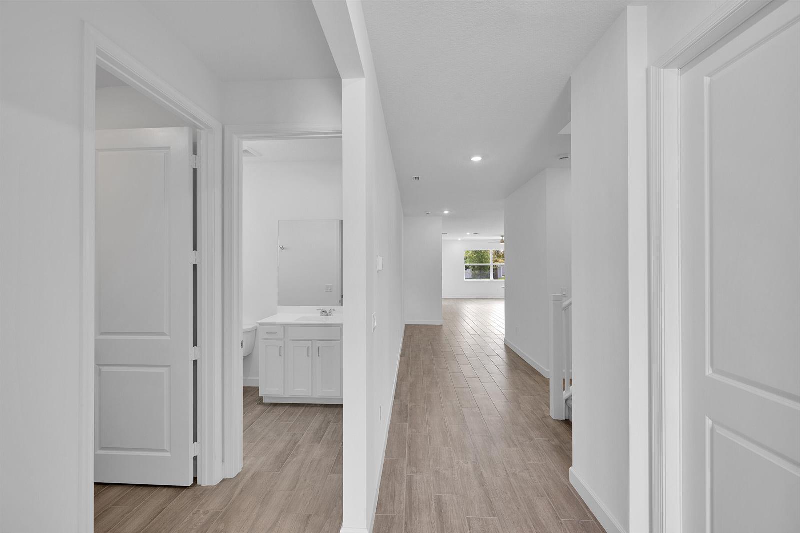 A hallway with wood-look tile flooring leads toward a bright room with a bathroom nearby — 5742 Graceful Way, Delray Beach FL 33484, DELRAY BEACH, FL