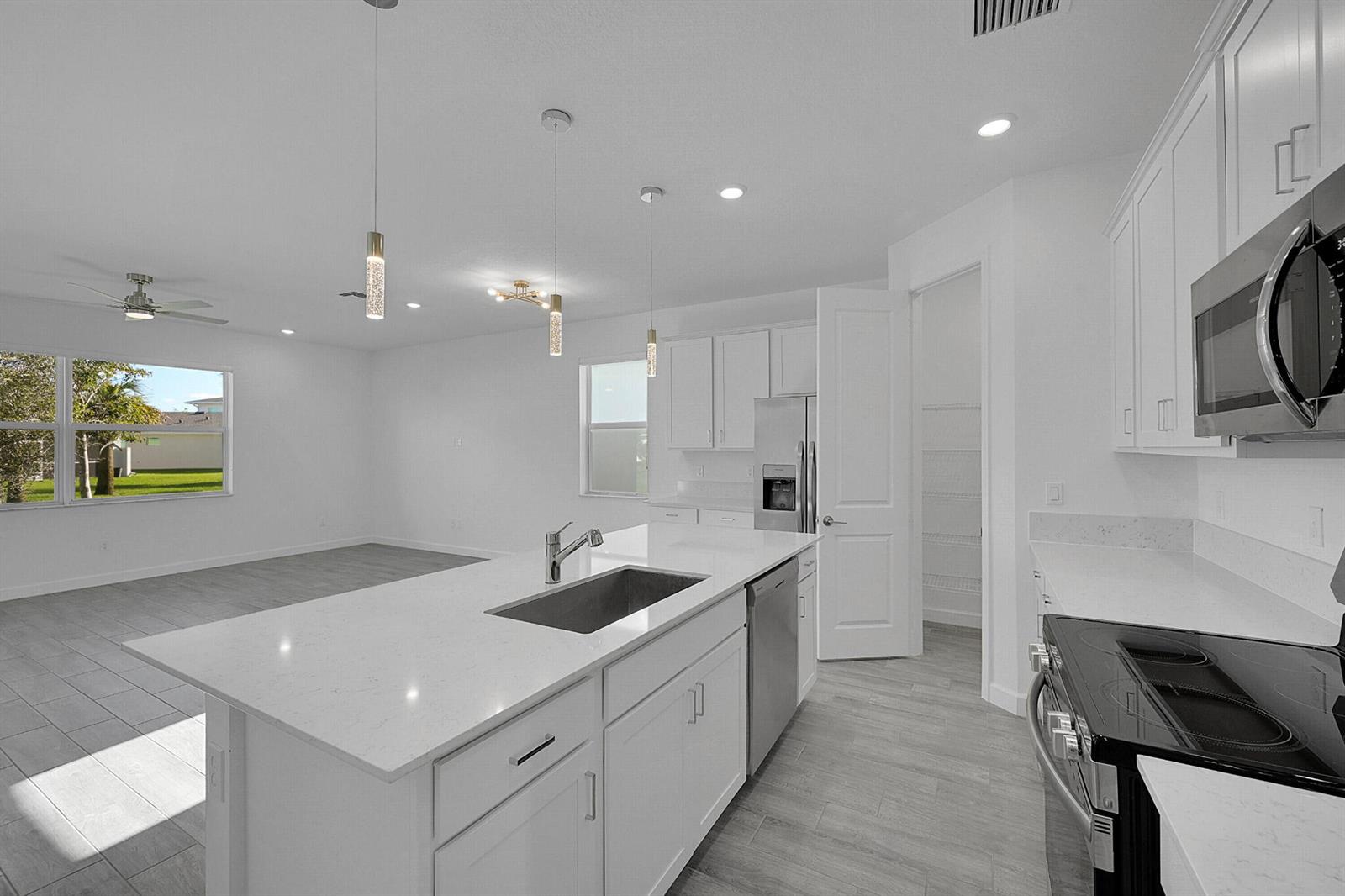 A modern kitchen features white cabinetry, a quartz island with a sink, and stainless appliances — 5742 Graceful Way, Delray Beach FL 33484, DELRAY BEACH, FL