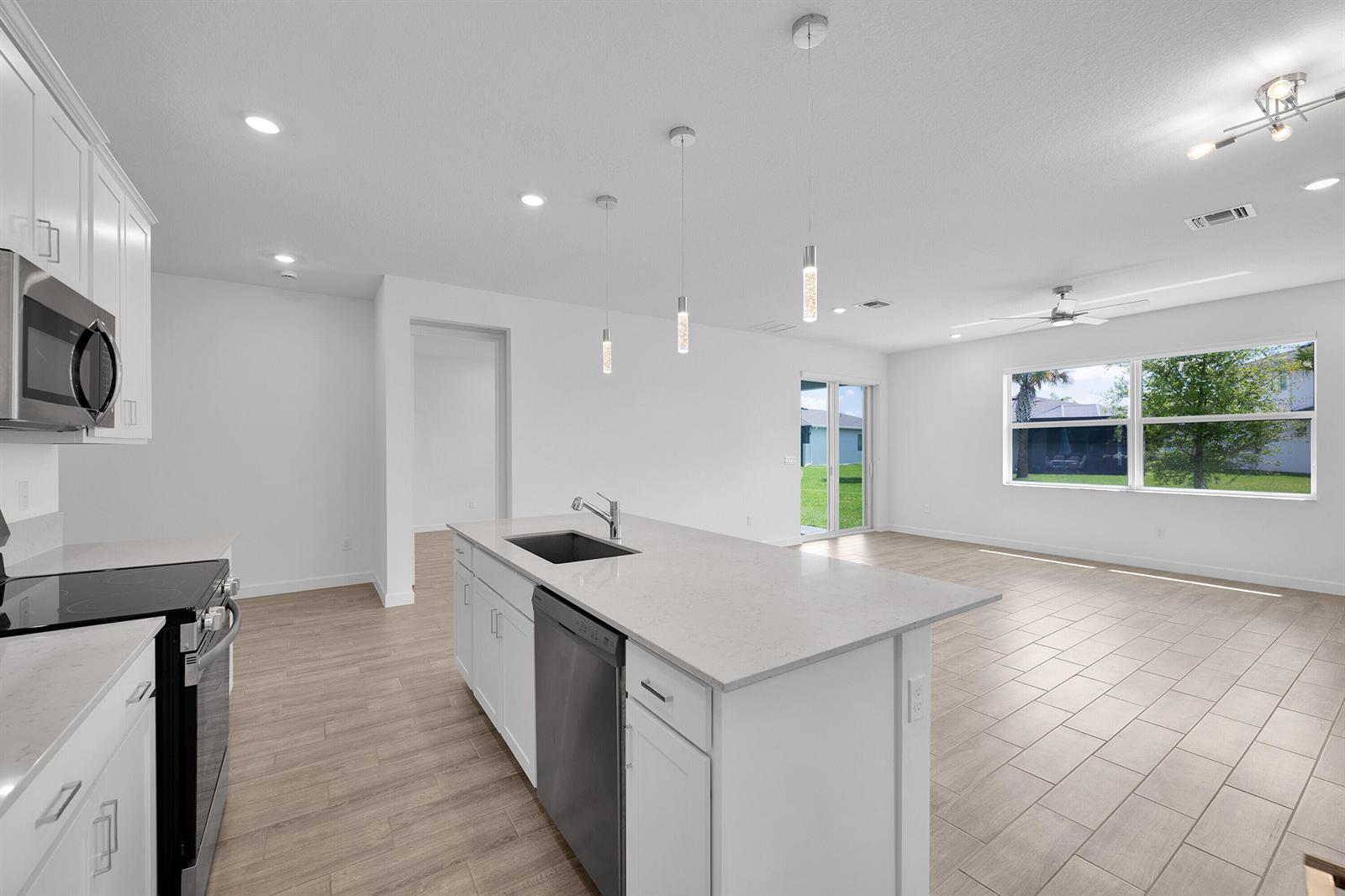 A modern kitchen with white cabinets, a central island, and tile flooring opens to a room — 5742 Graceful Way, Delray Beach FL 33484, DELRAY BEACH, FL