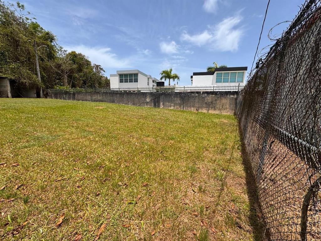 A grassy vacant lot is enclosed by a chain-link fence and a concrete wall — Carr 738 KM 1.4 BO MONTELLANO, CAYEY, PR