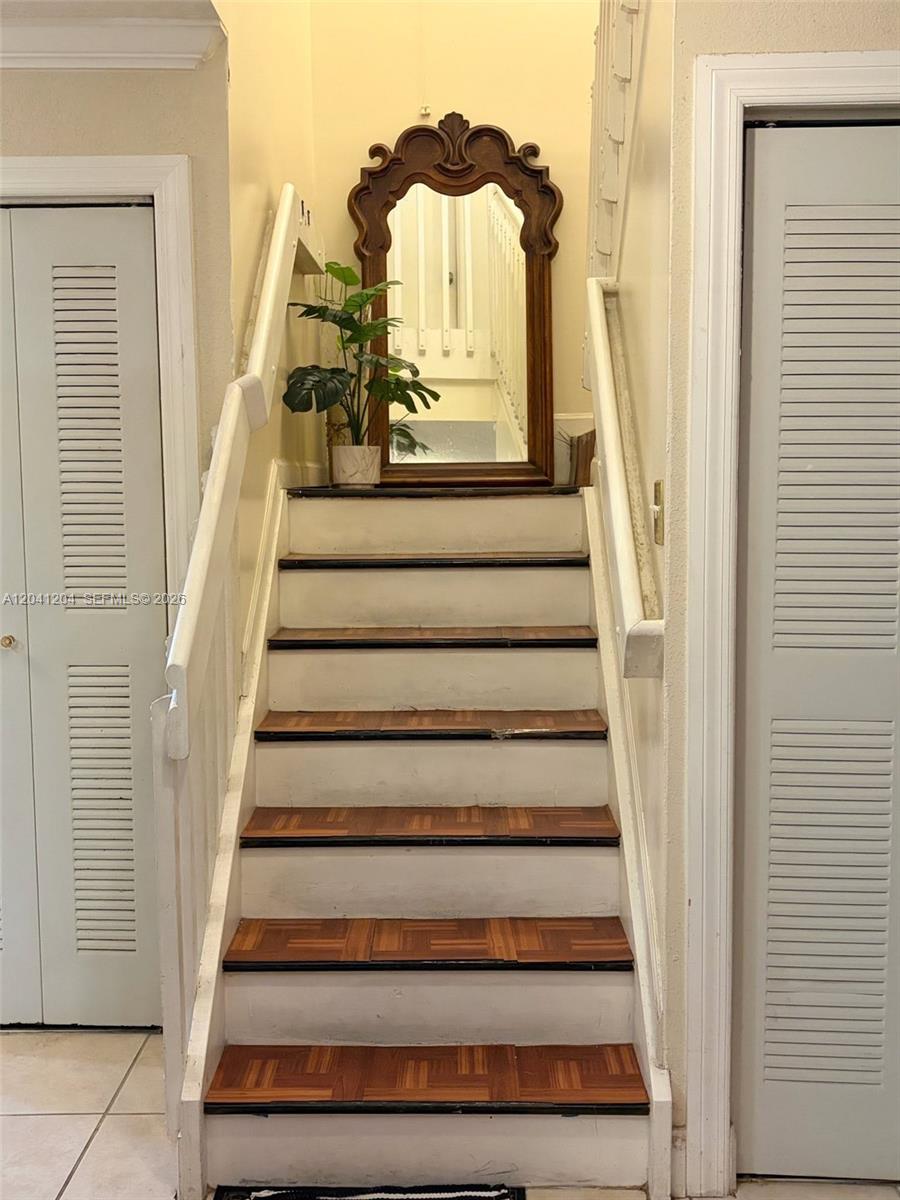 A staircase with wood-patterned treads and white risers features a large arched mirror — 13918 SW 172nd Ter, Miami FL 33177, MIAMI, FL