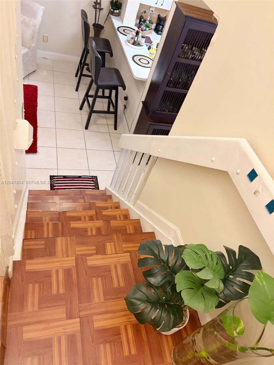 A view looking down a wooden staircase toward a kitchen with a breakfast bar — 13918 SW 172nd Ter, Miami FL 33177, MIAMI, FL