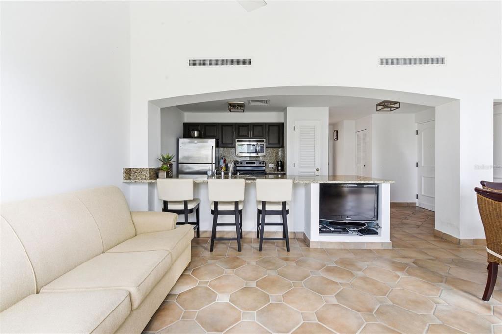 A kitchen with dark cabinets and granite countertops overlooks a living area with tile floors — Las Casitas I 1000 AVENUE EL CONQUISTADOR UNIT 5214-15-16, FAJARDO, PR