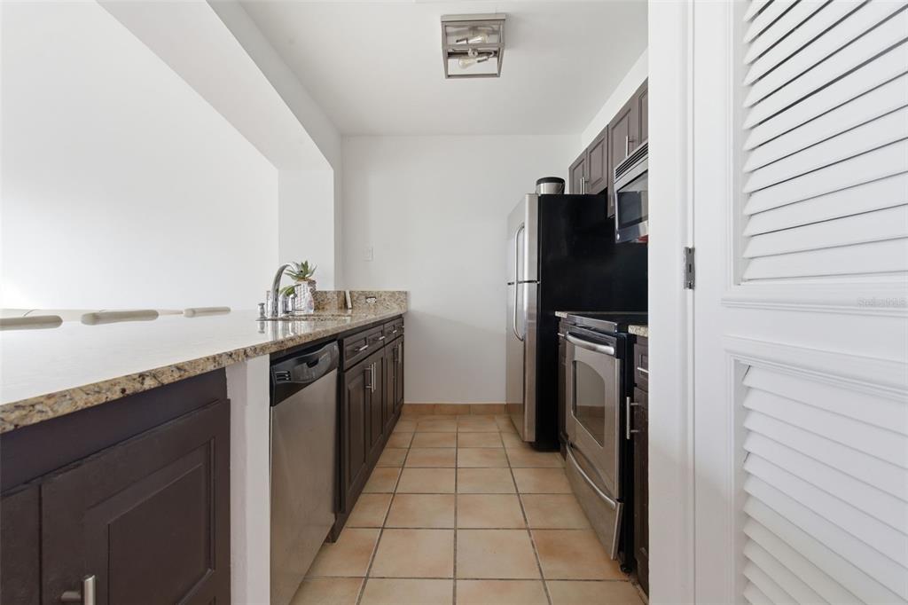 A galley kitchen features dark wood cabinets, granite countertops, stainless steel appliances, and tile flooring — Las Casitas I 1000 AVENUE EL CONQUISTADOR UNIT 5214-15-16, FAJARDO, PR