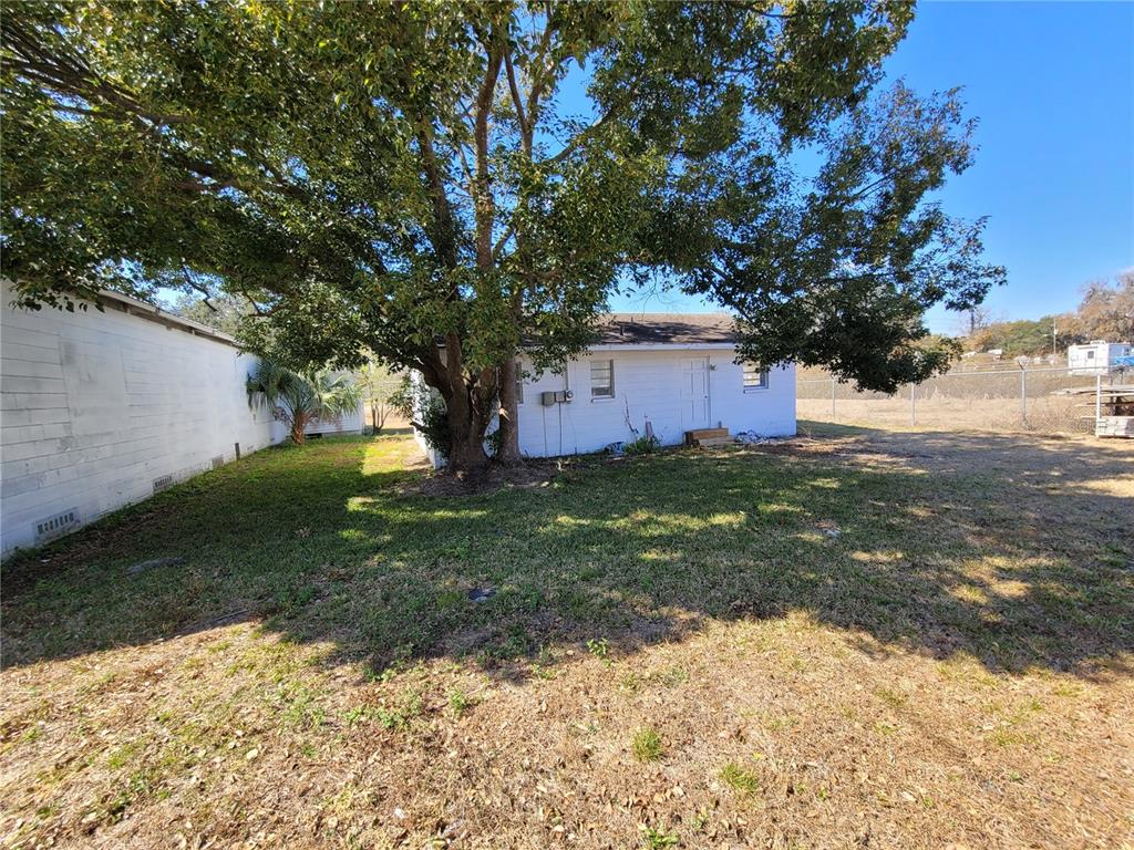 A white house exterior with a large tree in the yard and a side fence — 4830 GALL BOULEVARD, ZEPHYRHILLS, FL