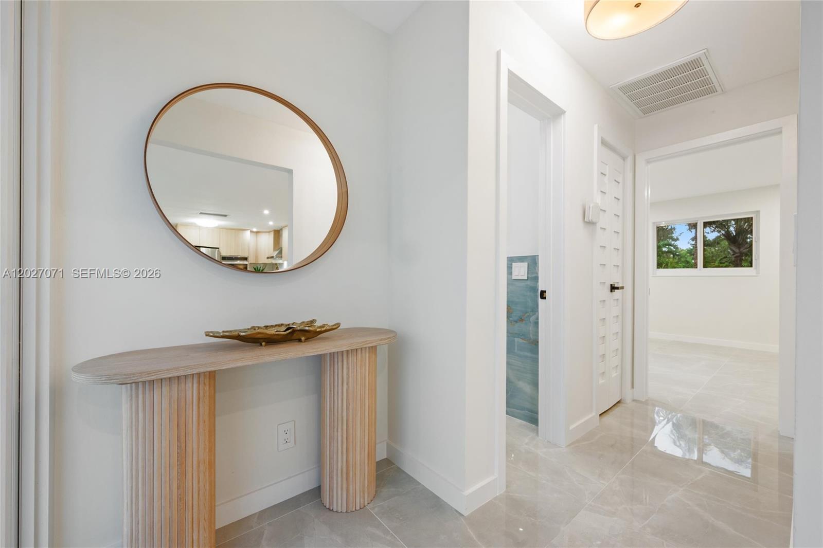 A hallway features a wooden console table, a round mirror, and light-colored tile flooring — 4024 Monroe St, Hollywood FL 33021, HOLLYWOOD, FL