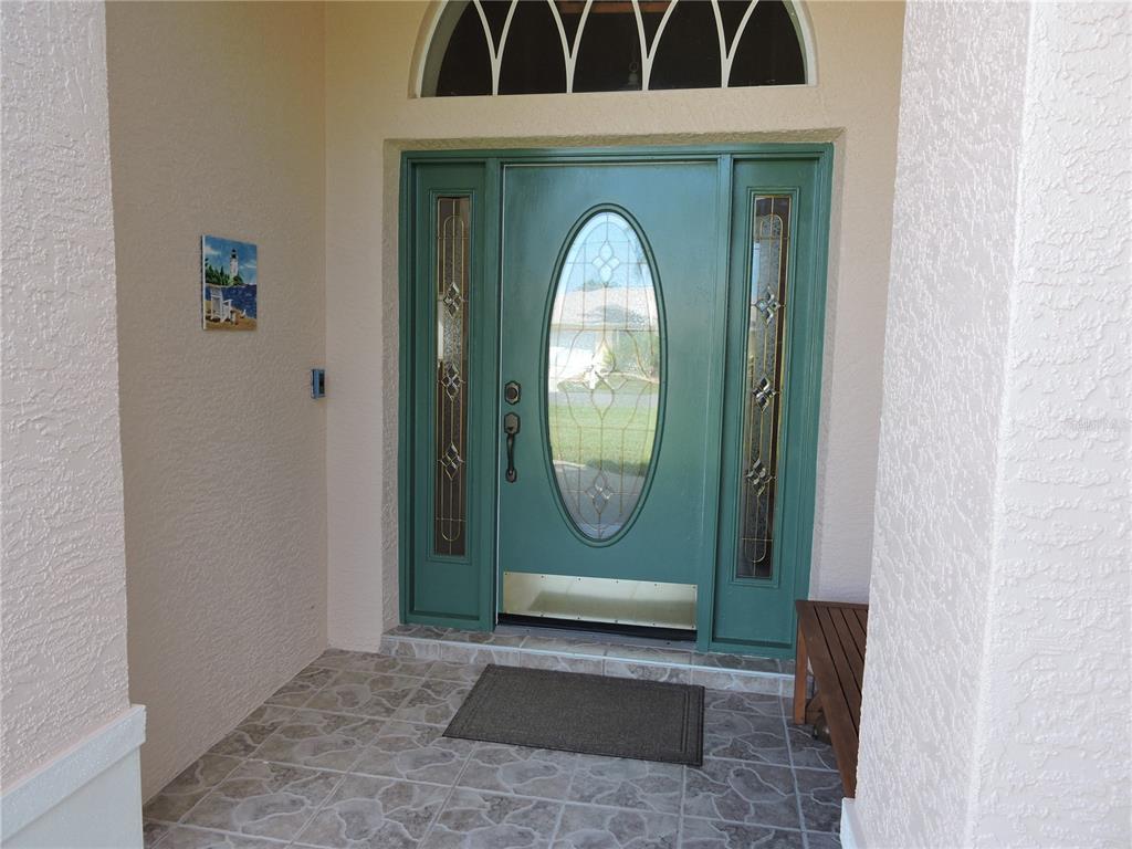 A teal front door with an oval glass insert and sidelights sits under a transom window — 110 MARINER LANE, ROTONDA WEST, FL