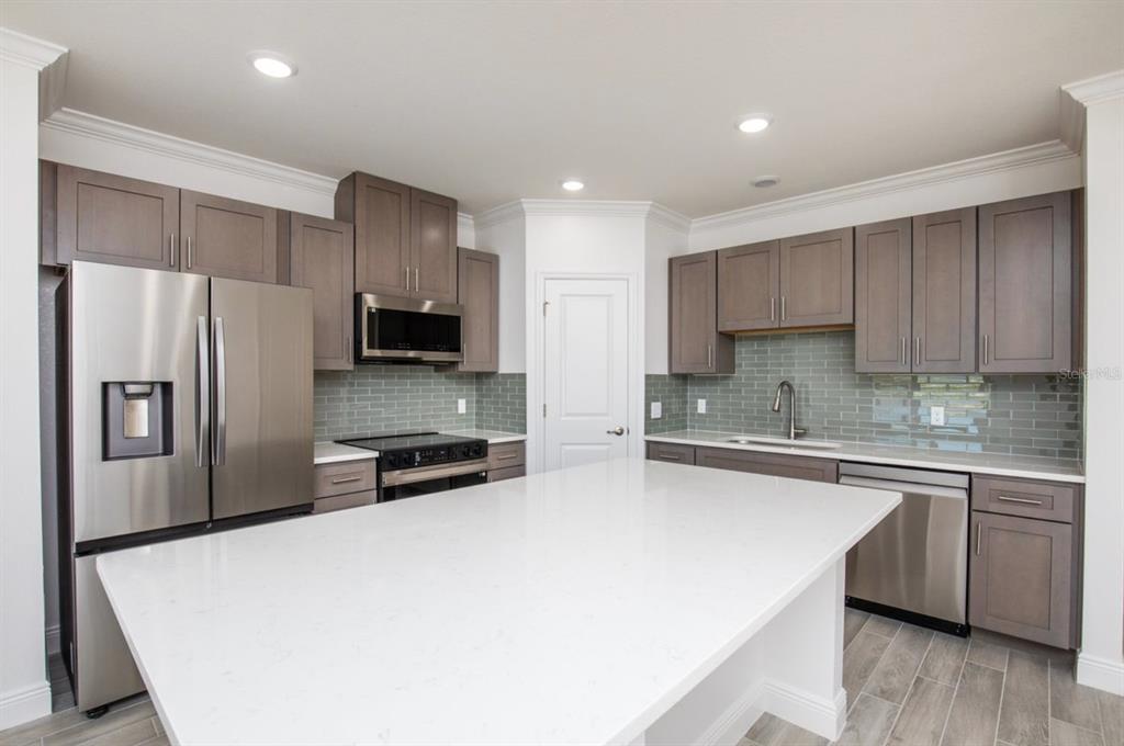 A modern kitchen features gray cabinets, stainless steel appliances, a white island, and tile backsplash — 10536 FOUNTAIN PALM CIRCLE, BOKEELIA, FL