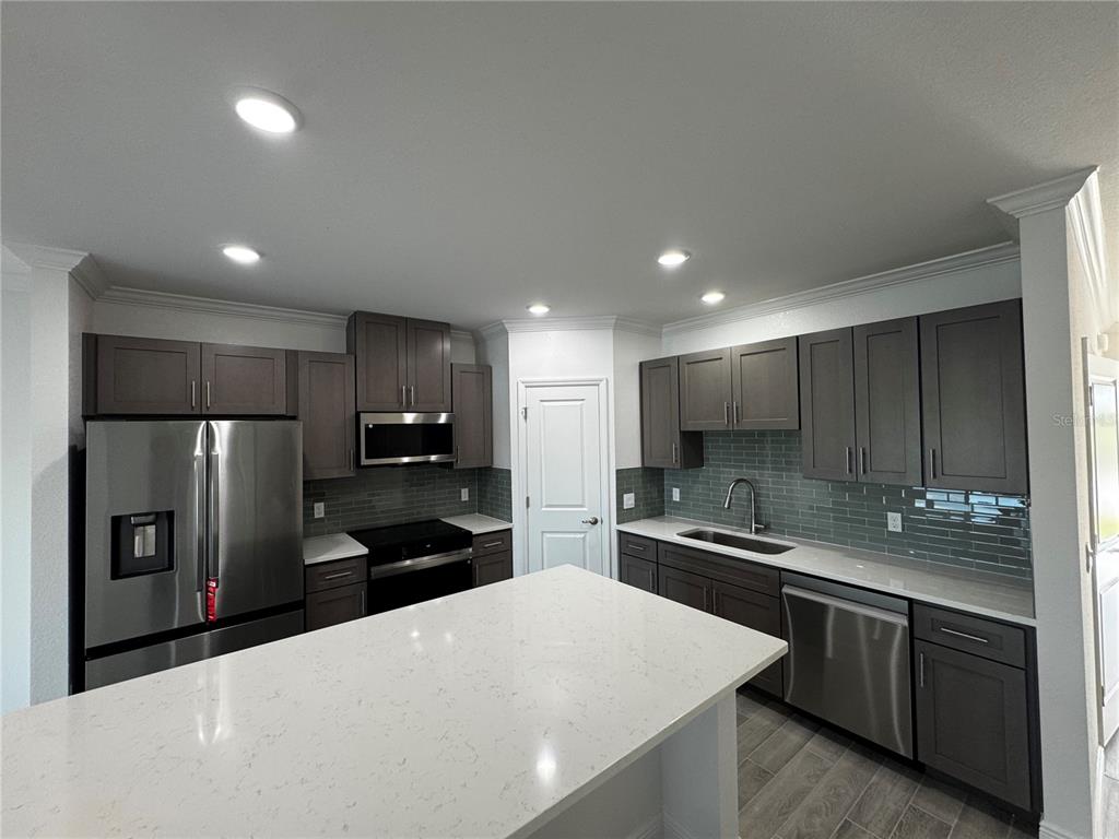 A modern kitchen features dark cabinetry, stainless steel appliances, and a white quartz island countertop — 10536 FOUNTAIN PALM CIRCLE, BOKEELIA, FL
