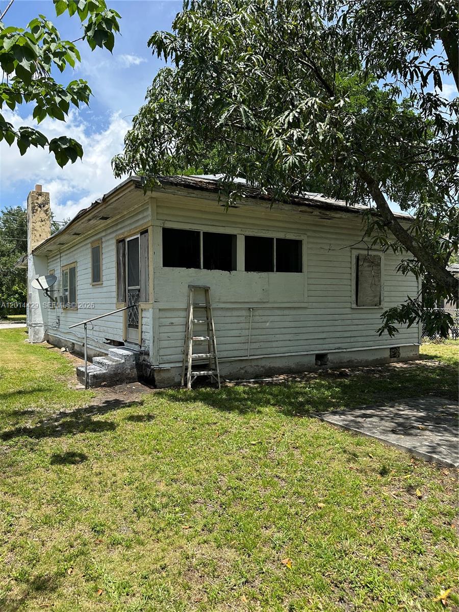 The exterior of a weathered, single-story house features white wood siding and a brick chimney — 3566 Thomas Ave, Miami FL 33133, MIAMI, FL