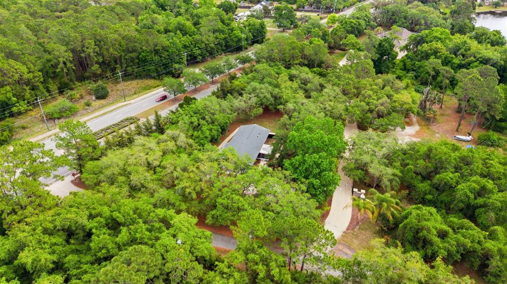 An aerial view shows a house nestled among dense trees near a road and lake — 176 LAKE EVA DRIVE, OVIEDO, FL