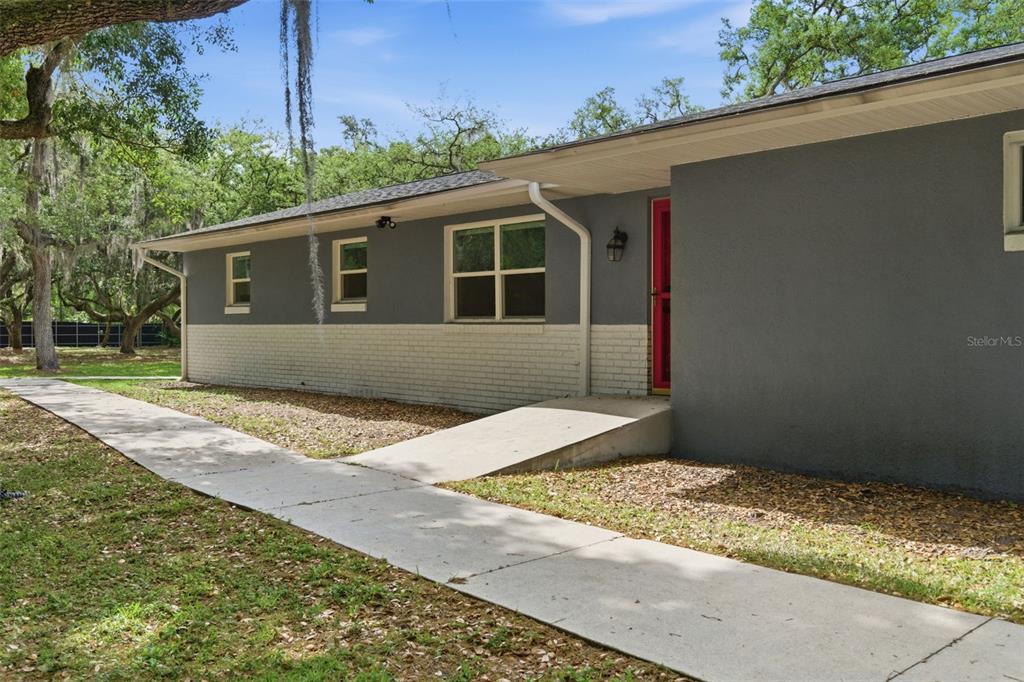 A gray house exterior features a white brick base, a concrete ramp, and a red door — 176 LAKE EVA DRIVE, OVIEDO, FL