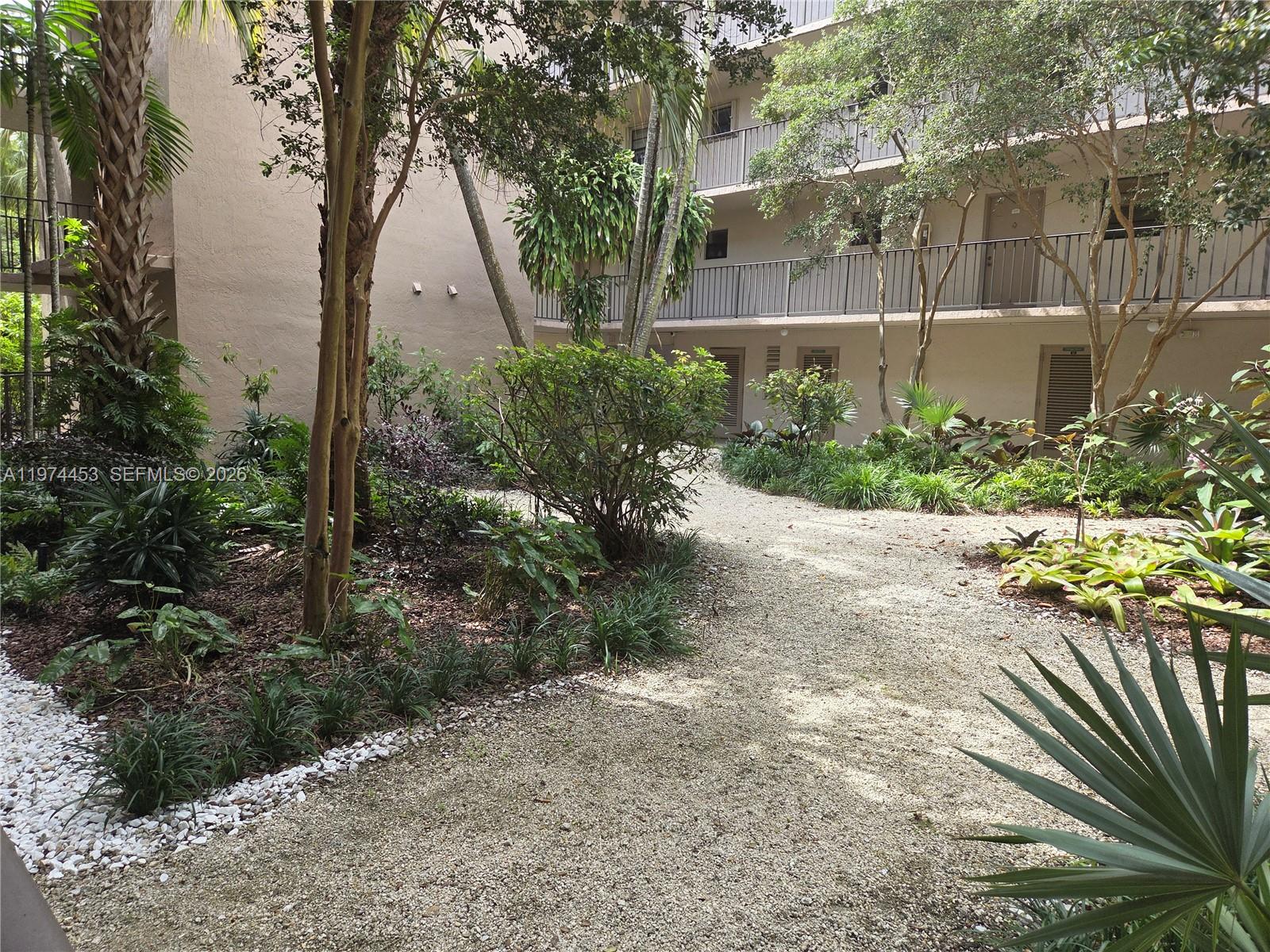 A gravel path winds through a landscaped courtyard between apartment building wings — 13020 SW 92nd Ave # A106, Miami FL 33176, MIAMI, FL