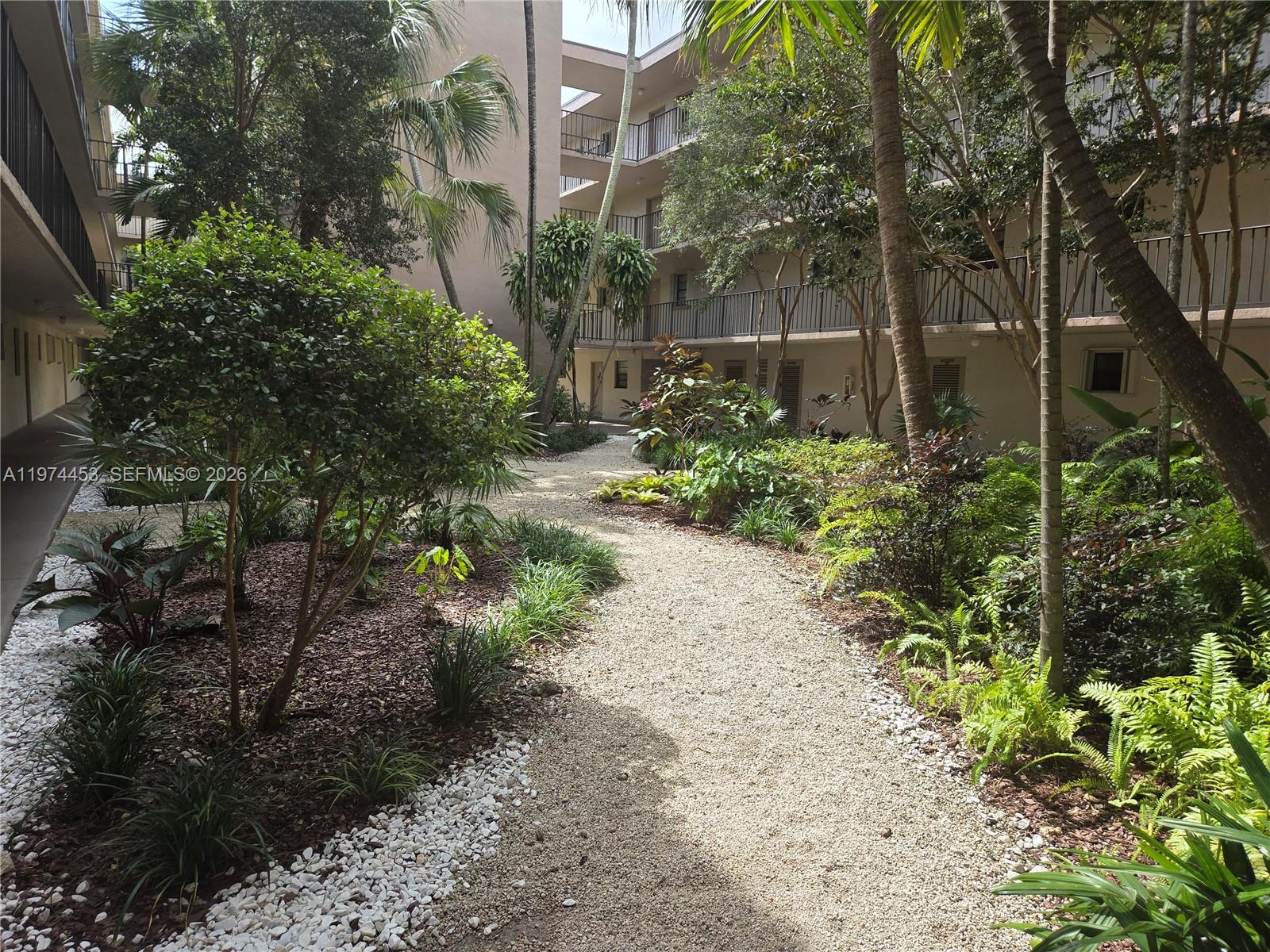 A gravel path winds through a landscaped courtyard between two multi-story apartment buildings — 13020 SW 92nd Ave # A106, Miami FL 33176, MIAMI, FL
