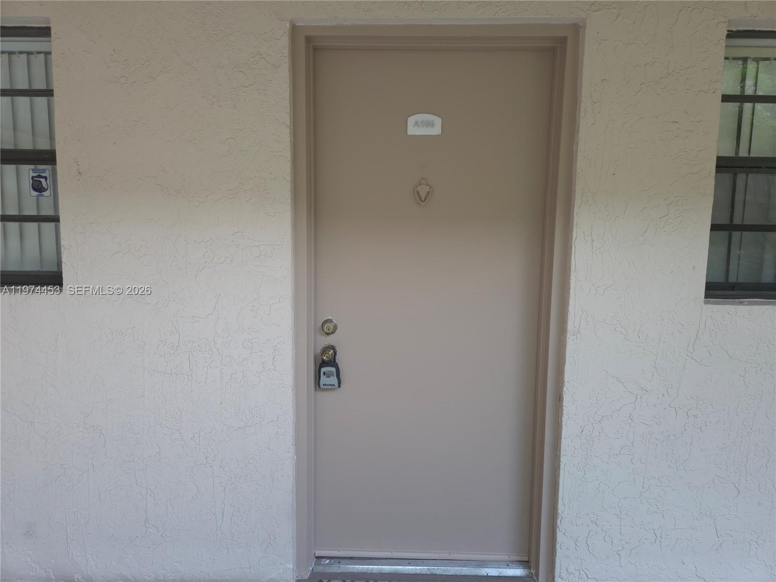 A beige exterior door with a lockbox is centered between two windows on a stucco wall — 13020 SW 92nd Ave # A106, Miami FL 33176, MIAMI, FL