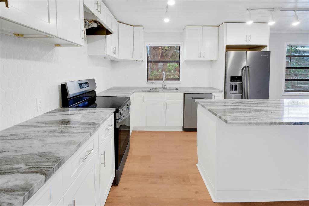 A modern kitchen features white cabinets, marble-patterned countertops, stainless steel appliances, and light wood flooring — 6425 S RICHARD AVENUE, TAMPA, FL