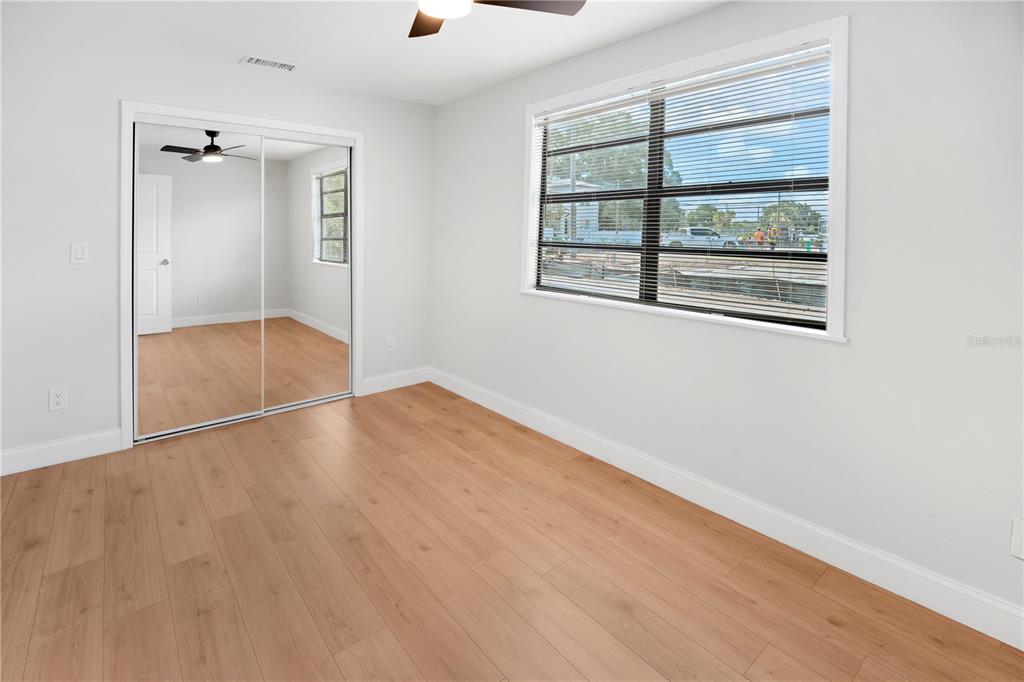 A bedroom with light wood-look flooring, white walls, a mirrored closet, and a large window — 6425 S RICHARD AVENUE, TAMPA, FL
