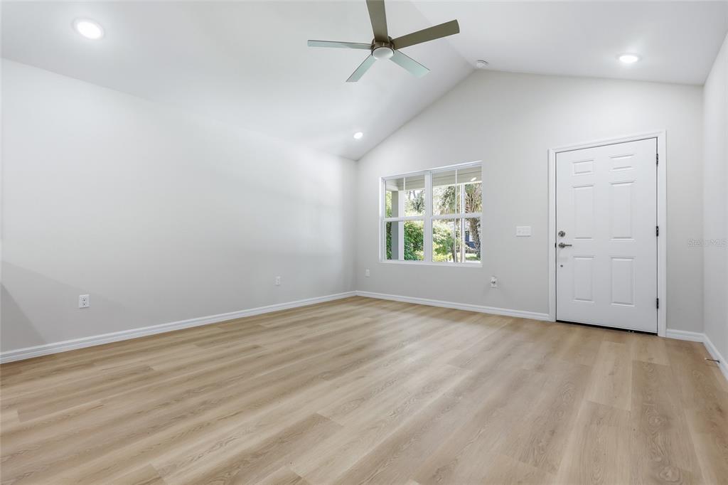 An empty room with light wood-look flooring, a vaulted ceiling, a ceiling fan, and a door — 2447 SE 10TH AVENUE, GAINESVILLE, FL