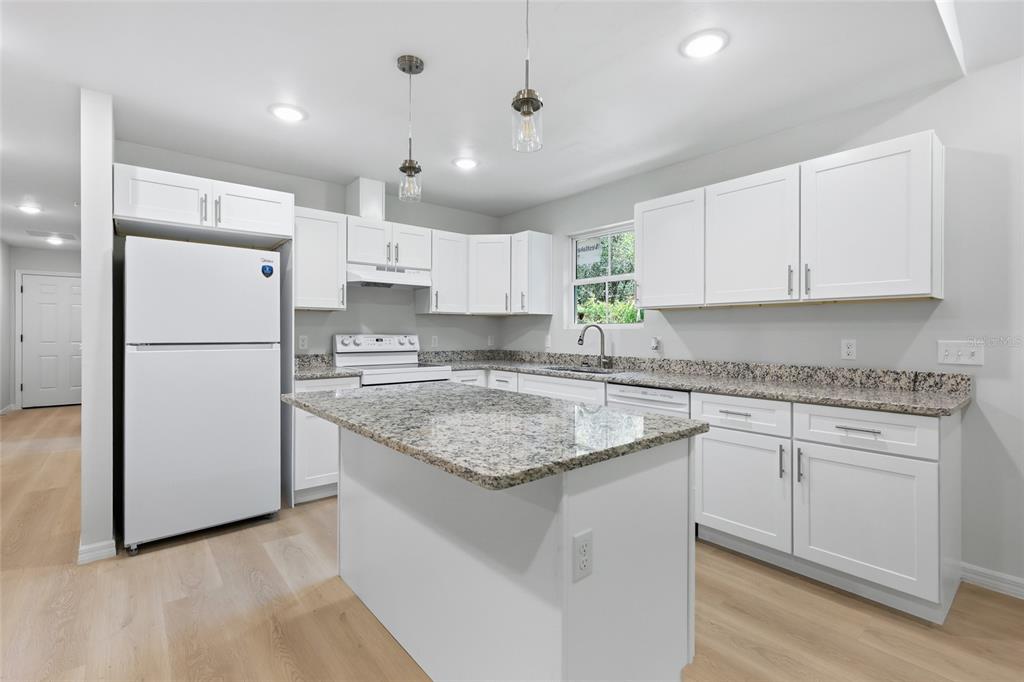 A kitchen features white cabinets, granite countertops, a central island, and light wood-look flooring — 2447 SE 10TH AVENUE, GAINESVILLE, FL