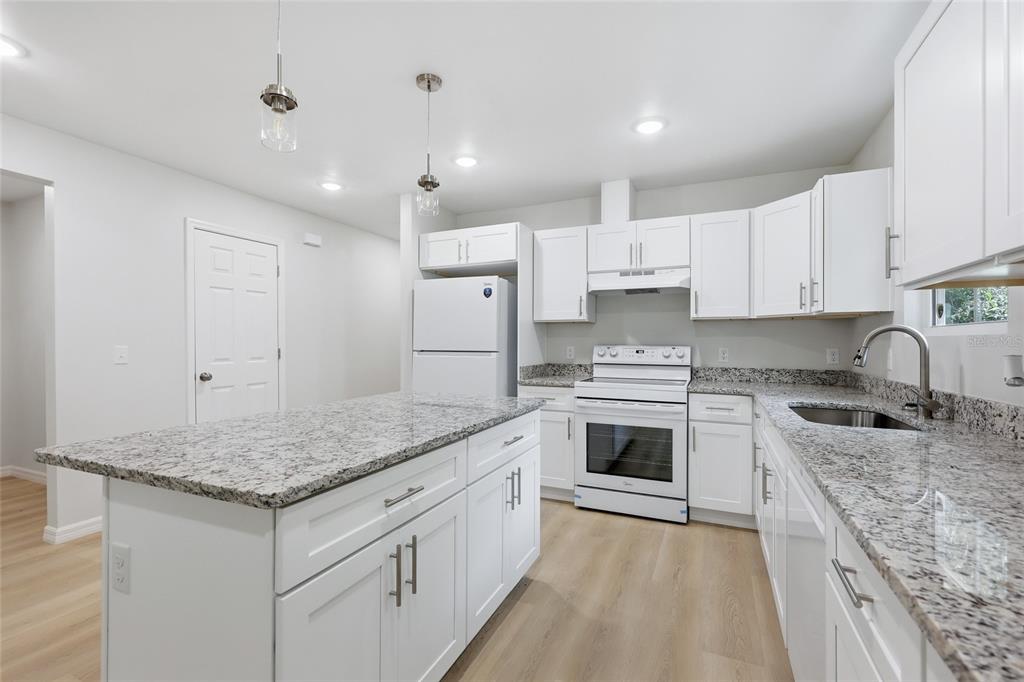 A kitchen features white cabinets, granite countertops, a kitchen island, and white appliances — 2447 SE 10TH AVENUE, GAINESVILLE, FL