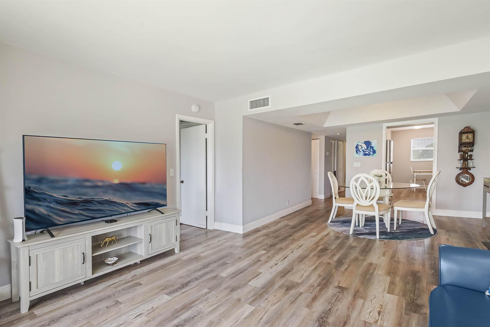 A living room with light wood-look flooring features a television on a white media console — 6850 10th Avenue N # 310, FL 33467, FL