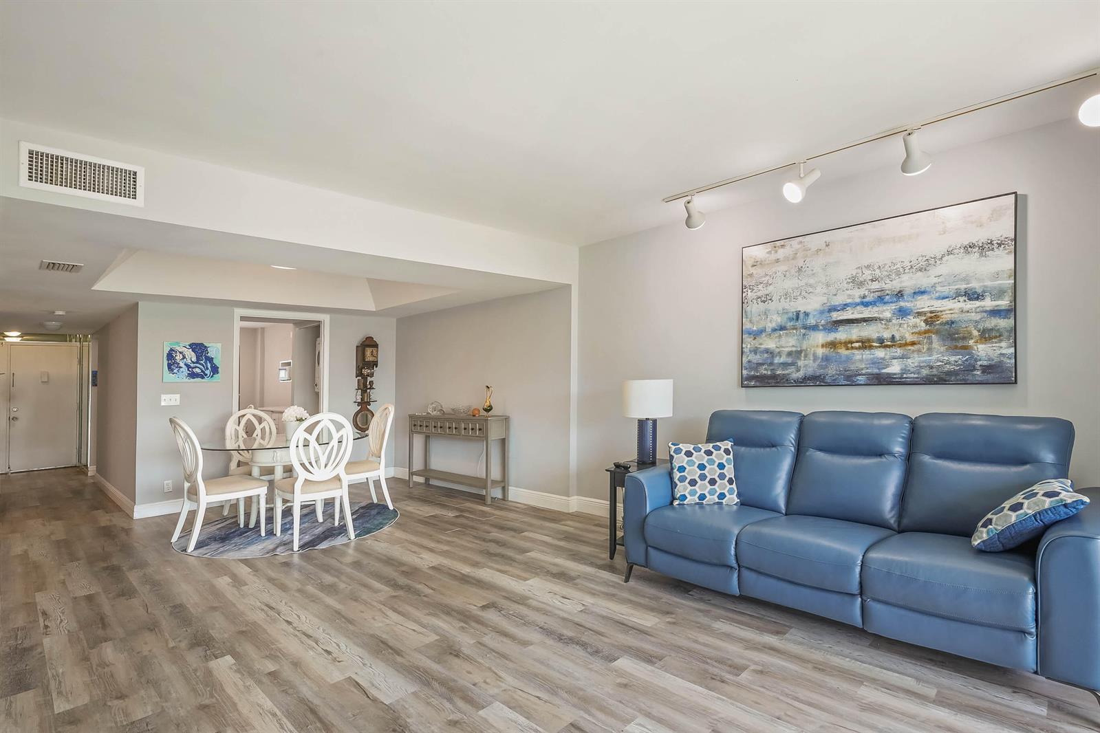 A living and dining area features light wood-look flooring, a blue sofa, and track lighting — 6850 10th Avenue N # 310, FL 33467, FL