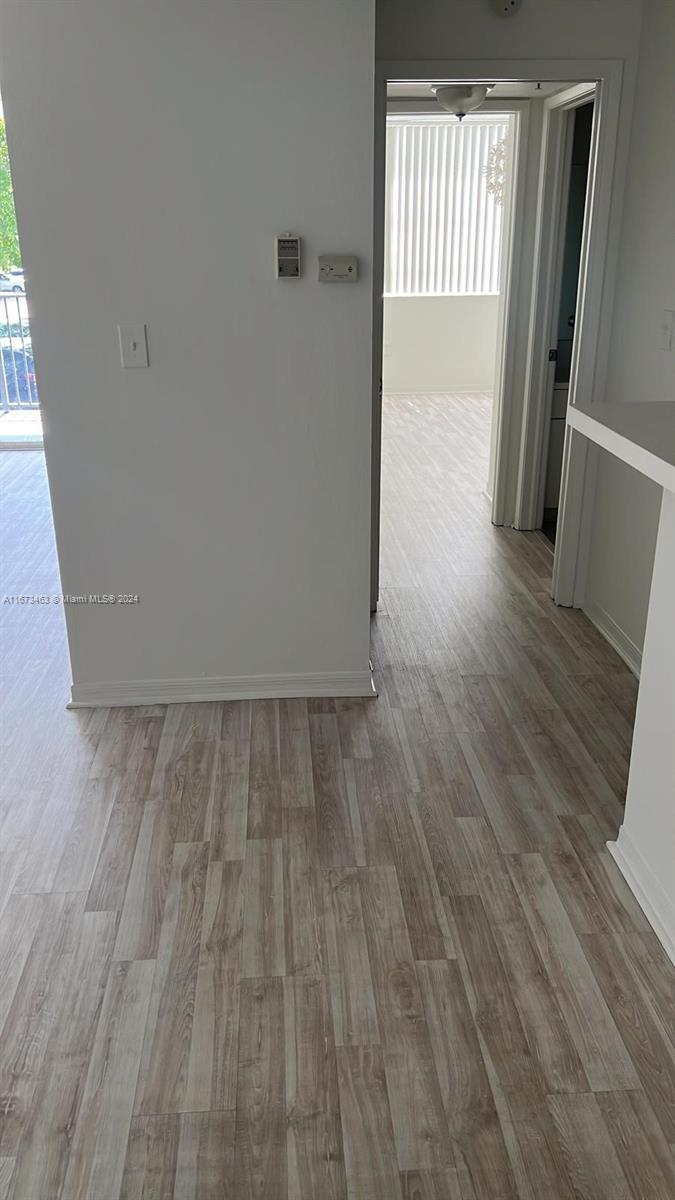 A hallway with light wood-look flooring leads to a doorway with vertical blinds — 4350 NW 107th Ave # 2, Doral FL 33178, DORAL, FL