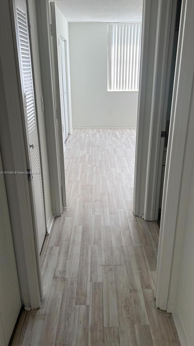 A narrow hallway with light wood-look flooring leads to a room with a window — 4350 NW 107th Ave # 2, Doral FL 33178, DORAL, FL