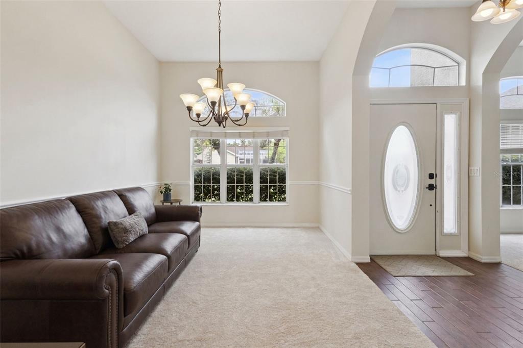 A living room with a brown leather sofa, beige carpet, chandelier, and white front door — 14313 ROXSHIRE DRIVE, ORLANDO, FL