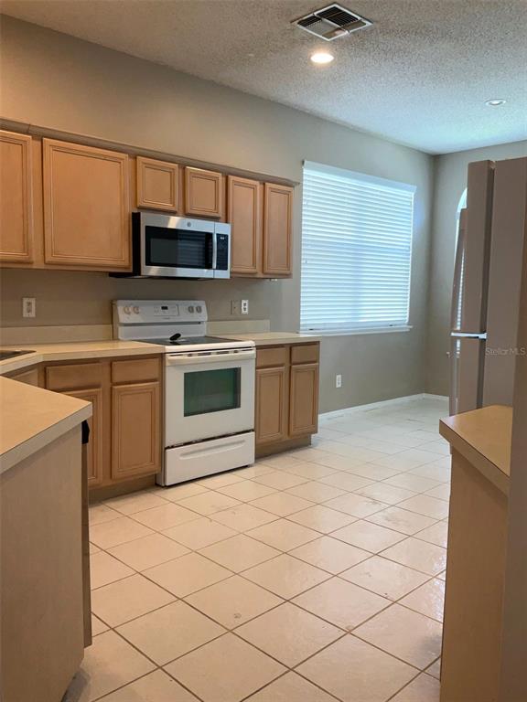 A kitchen features light wood cabinets, white appliances, and tiled flooring under a recessed light — 1318 LAKE BISCAYNE WAY, ORLANDO, FL