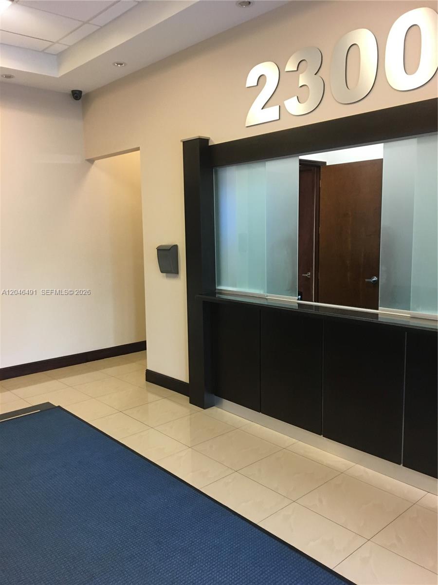 A reception area features a black service counter, a glass partition, and the number 2300 — 2300 W 84th St # 104, Hialeah FL 33016, HIALEAH, FL