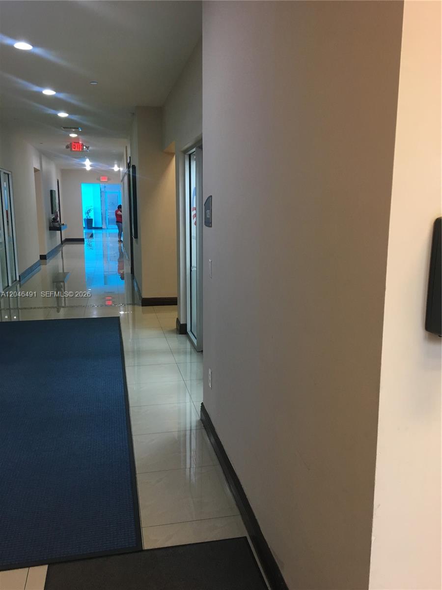 A long hallway features light-colored tile flooring, a blue runner rug, and glass office doors — 2300 W 84th St # 104, Hialeah FL 33016, HIALEAH, FL