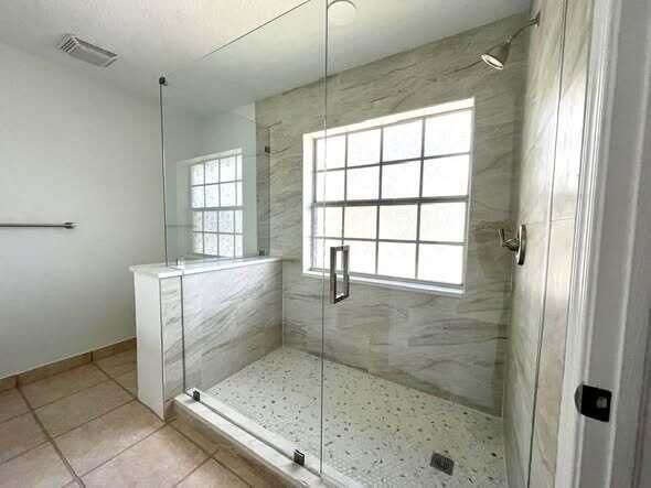 A walk-in shower features light-colored stone tile walls, a pebble floor, and glass enclosure panels — 1434 Hawthorne Place, Wellington FL 33414, WELLINGTON, FL