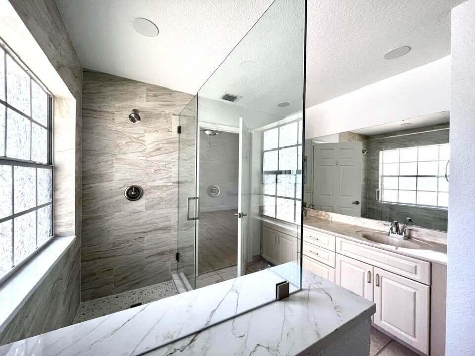 A bathroom features a glass-enclosed walk-in shower with stone-look tile and a marble-topped vanity — 1434 Hawthorne Place, Wellington FL 33414, WELLINGTON, FL