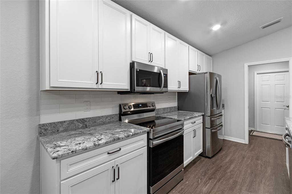 A kitchen features white cabinets, granite countertops, stainless steel appliances, and wood-look flooring — 2311 SUNSET WAY, DAVENPORT, FL