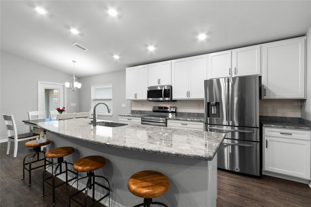 A kitchen features white cabinets, granite countertops, a large island with bar stools, and stainless appliances — 2311 SUNSET WAY, DAVENPORT, FL
