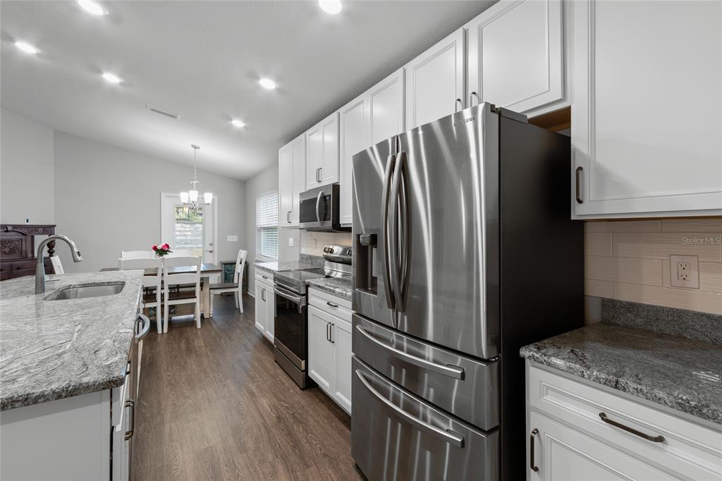 A kitchen features white cabinets, granite countertops, stainless steel appliances, and a dining area nearby — 2311 SUNSET WAY, DAVENPORT, FL