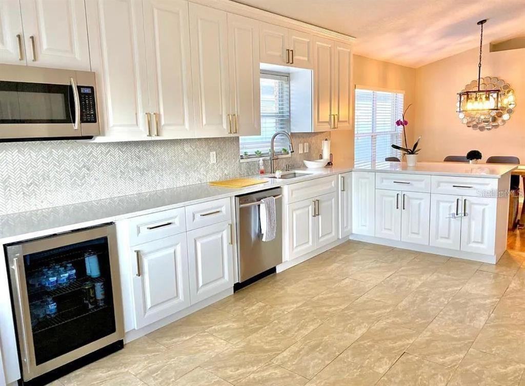 A kitchen features white cabinets, stainless steel appliances, a herringbone backsplash, and light tile flooring — 31352 GOLDEN GATE DRIVE, WESLEY CHAPEL, FL