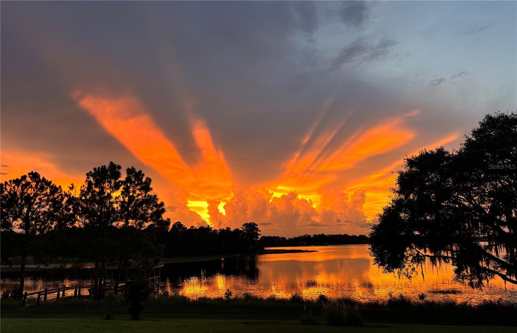 A vibrant sunset glows over a lake with silhouetted trees in the foreground — 8750 BAYVIEW CROSSING DRIVE, WINTER GARDEN, FL