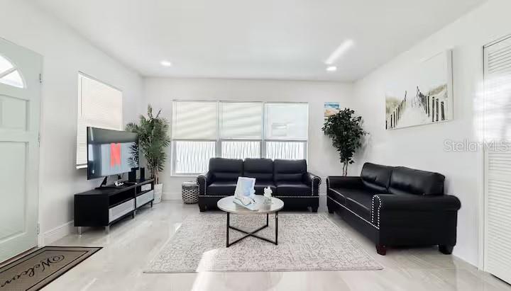 A bright living room features black leather sofas, a television, and a neutral area rug — 13912 DULEY AVENUE, HUDSON, FL