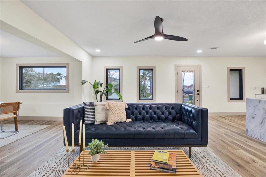 A living room features a navy tufted sofa, a slatted coffee table, and a ceiling fan — 203 DRIFTWOOD DRIVE W, PALM HARBOR, FL