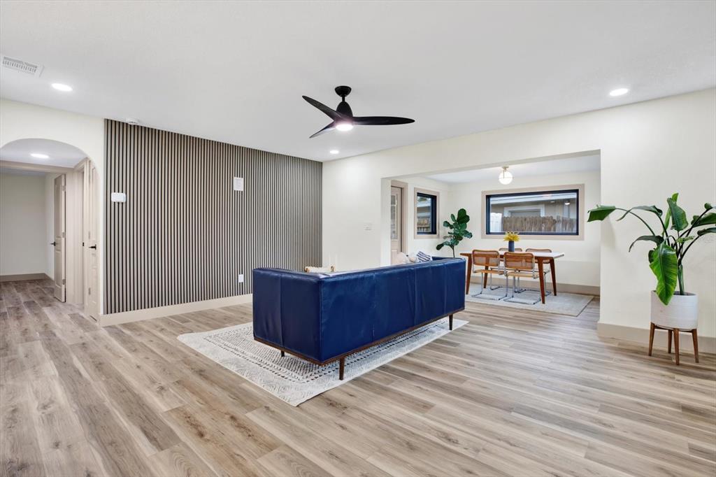 A living room with wood-look flooring, a blue sofa, and a vertical slat accent wall — 203 DRIFTWOOD DRIVE W, PALM HARBOR, FL