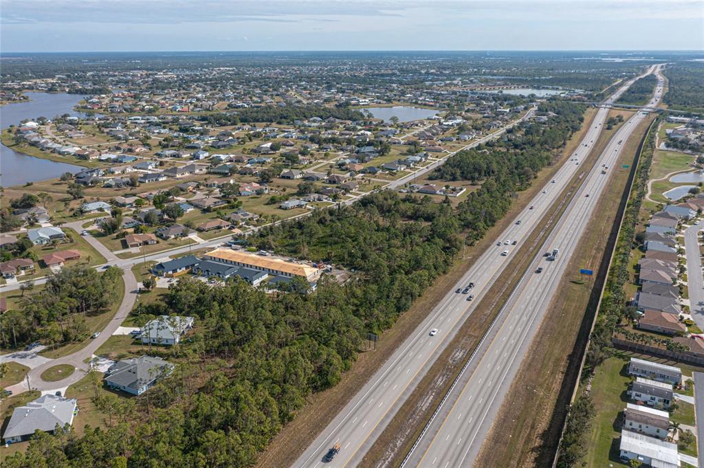 An aerial view shows a highway running alongside a residential neighborhood with several lakes — 24511 ZEPHYR COURT, PUNTA GORDA, FL